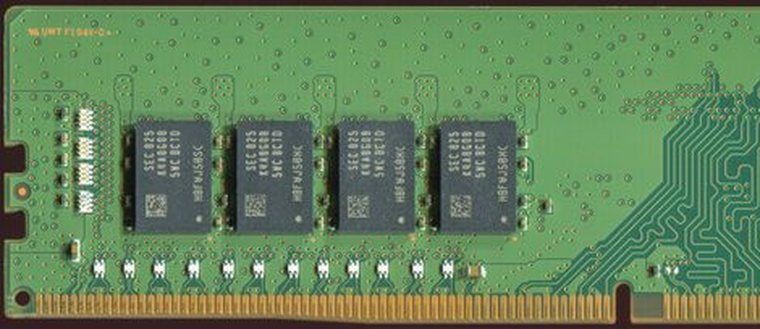 Close-up of a DDR4 memory module: four black memory chips on a green circuit board, above the gold contact edge.